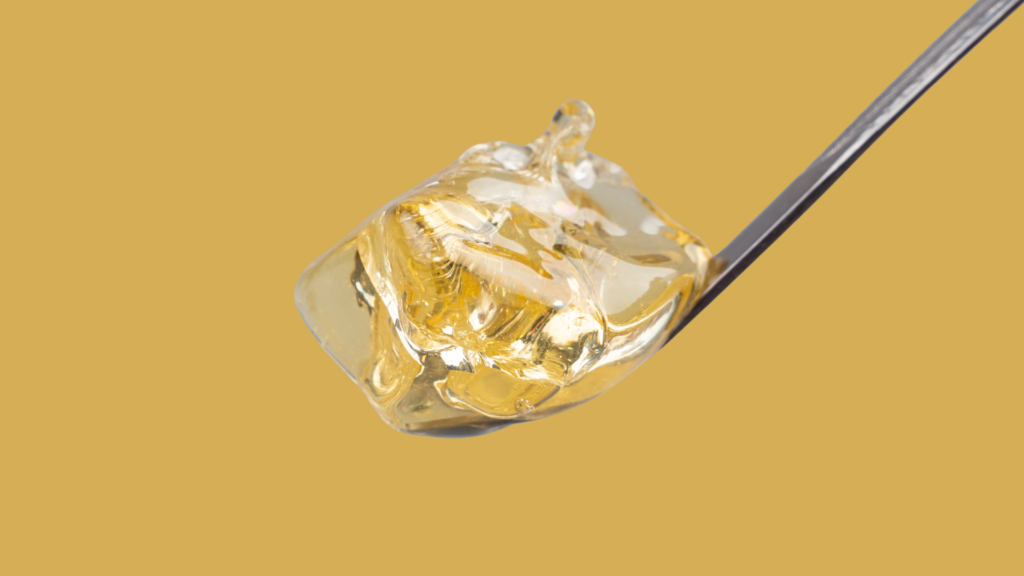 Clear golden cannabis concentrate on the tip of a dab tool against a warm gold background.