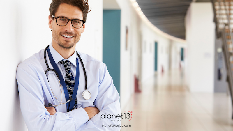 Male doctor wearing glasses and a white coat in a hospital hallway.