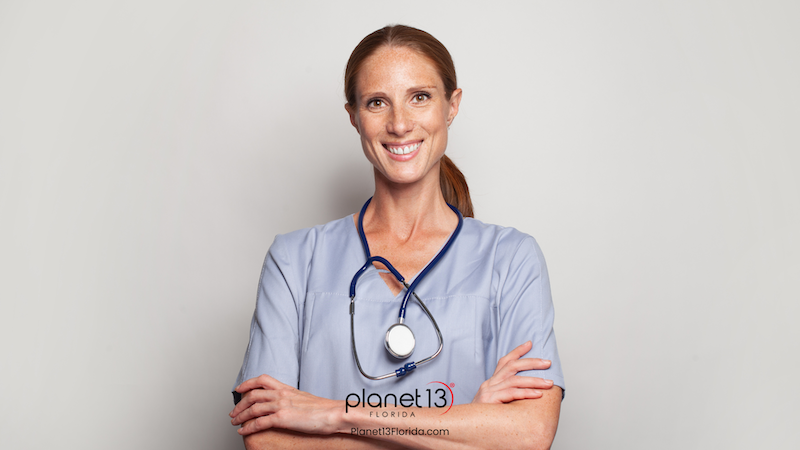 Female healthcare professional wearing blue scrubs against a light background.
