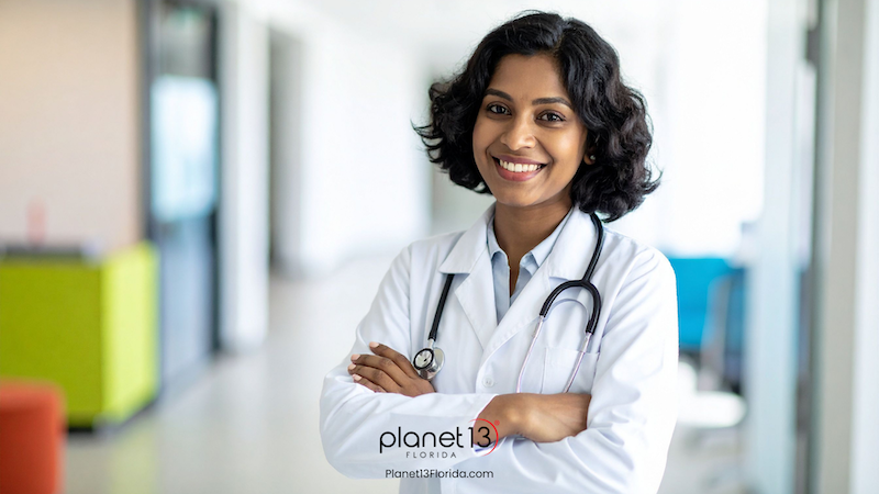 Female doctor wearing a white coat and stethoscope in a bright medical office.