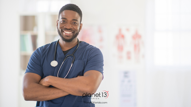 Smiling male healthcare professional wearing dark blue scrubs and a stethoscope.